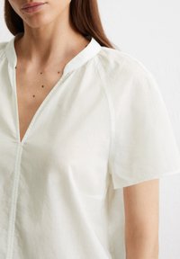 Weiße, leichte Bluse mit kurzen Ärmeln, einem V-Ausschnitt und subtiler Textur. Verfügt über geraffte Schultern und eine gerade Silhouette.