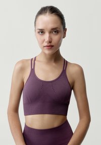 Sujetador deportivo morado con un diseño sin costuras, tirantes finos, tela texturizada y sutiles patrones geométricos en la parte frontal.