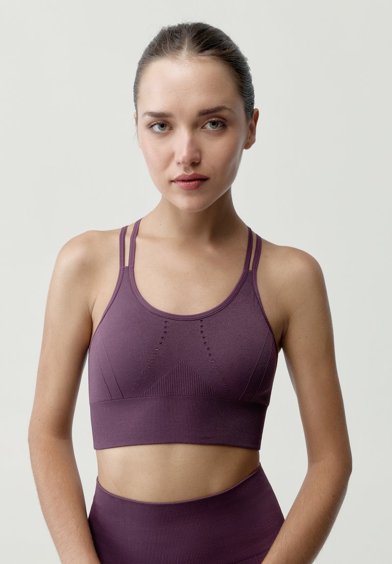 Sujetador deportivo morado con un diseño sin costuras, tirantes finos, tela texturizada y sutiles patrones geométricos en la parte frontal.