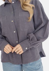 Szara, teksturowana koszula z guzikami, z dwiema kieszeniami na piersi, perłowe guziki i luźne rękawy, w połączeniu z jasnoniebieskimi dżinsami.