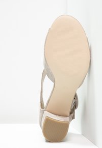 Scarpa con tacco alto in suede beige, con suola texturizzata, apertura sul retro e cinturino alla caviglia, caratterizzata da un tacco a blocco e un interno liscio di colore neutro.