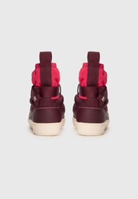 Ett par röda och vinröda hög-top sneakers med gräddfärgade sulor, visade bakifrån på en vit bakgrund.