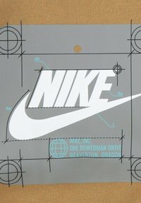 Logo Nike su uno sfondo grigio con contorno nero. Presenta disegni tecnici e testo turchese, incluso un'icona del globo e dettagli dell'indirizzo.