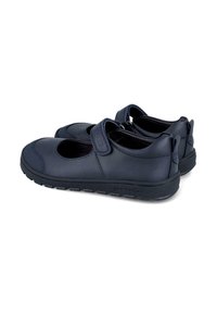 Zapatos negros estilo Mary Jane con punta redonda, correas ajustables de Velcro y suelas de goma, mostrados desde un ángulo lateral y trasero.