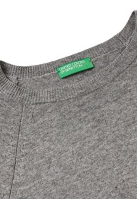 Šedý pletený svetr s výstřihem a viditelným švem, na němž je zelená etiketa s nápisem "United Colors of Benetton".