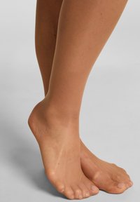 Huidskleurige sheer panty op voeten, met een gladde textuur en een natuurlijke uitstraling. Kleurverlopen vloeien naadloos over in de huid.