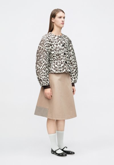 Κοντό σακάκι με λεοπάρ μοτίβο και κούμπωμα με κουμπιά, μπεζ φούστα με καρό λεπτομέρεια, ανοιχτό γκρι κάλτσες και μαύρα παπούτσια.