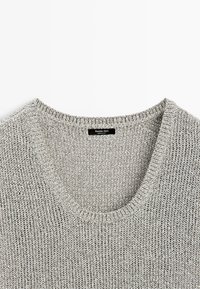 Gros plan sur l'encolure d'un pull tricoté gris clair avec une étiquette noire indiquant « Massimo Dutti, Made in Italy ».