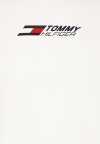 T-shirt bianca in cotone con un logo stampato multicolore: testo nero "TOMMY" sopra "HILFIGER", con una striscia orizzontale rossa, bianca e blu.