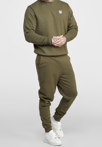 Olivgrön sweatshirt och matchande joggers i mjukt tyg, med en liten vit logotyp på bröstet och elastiska mudd vid anklarna.