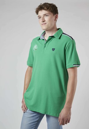 Polo vert en coton avec col, logo brodé et accents contrastants en bleu marine sur les épaules.
