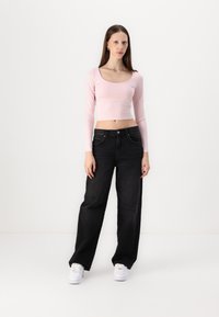 Svijetloružičasti dugih rukava crop top, crne široke traperice i bijele tenisice. Glatka tkanina, prilagođen dizajn i visoki struk s džepovima.