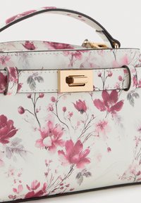 Bolso con fondo blanco, estampado floral rosa, broche rectangular dorado y correa a juego con flores, unida al asa superior.