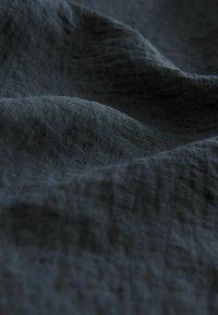 Tmavě šedá látka s texturovaným, mírně pomačkaným povrchem, vykazující jemné variace v odstínu a měkký, lehký vzhled.