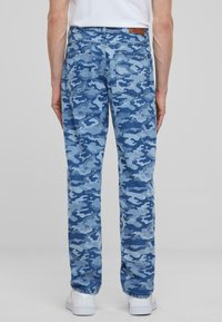 Blue camouflage denim jeans featuring a straight leg cut, rear pockets, and a tan leather label at the waistband.