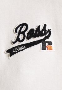 Écusson texturé noir et blanc avec le texte « Boss Athletic » et un petit logo brodé noir, blanc et orange sur fond de tissu blanc.