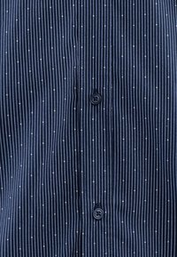 Marineblaue Bluse mit dünnen vertikalen Streifen und weißen Punkten, mit Knopfschluss und glattem Stoff.