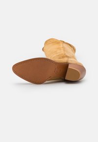 Beżowe zamszowe botki za kostkę z niewielkim obcasem, z gładką skórzaną podeszwą oraz subtelnym przeszyciem wzdłuż krawędzi.