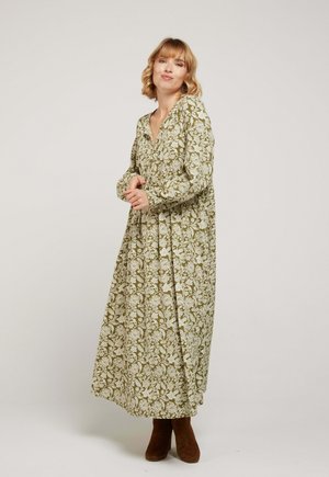 Robe florale longue de couleur olive avec des manches longues, un décolleté en V et une silhouette fluide, complétée par des bottines marron.