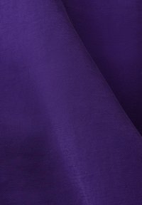 Gros plan d'un tissu violet plié avec une texture côtelée diagonale et une apparence lisse et douce.