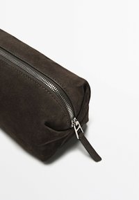 Bruin suède zakje met een zilveren ritssluiting. Vierkante vorm, gladde textuur, met een klein leren tabje. Minimalistisch ontwerp.