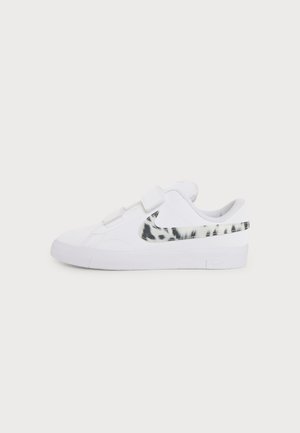 Baskets basses blanches avec un swoosh Nike marbré noir et blanc, des sangles velcro et une semelle blanche plate, vues de côté extérieur.