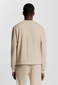 Felpa beige con maniche lunghe, scollo rotondo e texture morbida. Presenta una vestibilità rilassata e polsini a costine, progettata per il comfort.