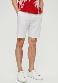 Shorts en coton blanc avec poches latérales, coupe décontractée, associés à des baskets blanches. Le haut présente un motif graphique rouge.
