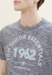 Šedý melange T-shirt s kulatým výstřihem. Obsahuje modrý grafický text "1962" a "TOM TAILOR ESSENTIALS" v kontrastní bílé barvě.