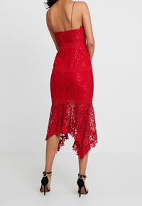 Robe en dentelle rouge avec des bretelles spaghetti, dotée d'un corsage ajusté, d'un ourlet à volants et de bords festonnés. Porte avec des escarpins à bride de cheville noirs.