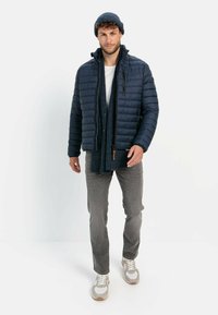 Navy puffer jacket with corrugated texture, zip closure, paired with a dark knitted scarf and grey pants, featuring white sneakers.