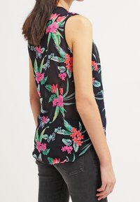 Blusa sin mangas de tela negra con un vibrante estampado floral en rosa, verde y púrpura. Presenta un corte relajado y un dobladillo curvado.