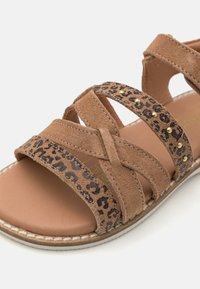 Brune sandaler med kryssede stropper, med leopardmønstrede detaljer og gullstifter. Myk semsket tekstur, polstret såle og hvit søm.