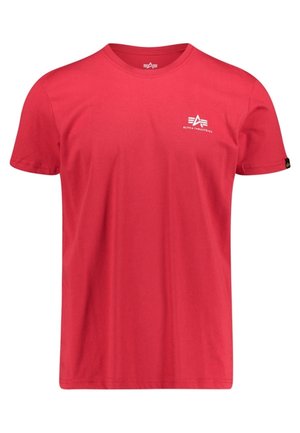 Czerwona koszulka z krótkim rękawem i okrągłym dekoltem, z małym białym logo Alpha Industries na lewej piersi oraz czarną metką na lewym rękawie.