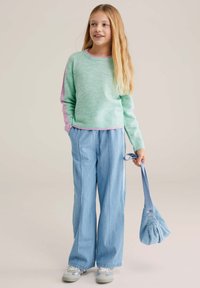 Pull vert menthe avec des accents roses, associé à un pantalon large bleu clair et un petit sac bleu. La tenue présente des textures douces et un design décontracté.