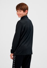 Svart långärmad skjorta med hög krage, tillverkad av slät tyg; har en avslappnad passform och subtilt konturerad rygg.