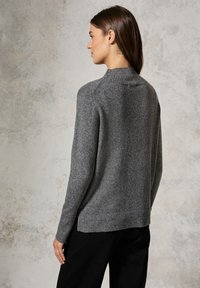 Szary sweter dzianinowy z prążkowanymi kołnierzykiem i mankietami, o lekko luźnym kroju i dłuższym tylnym dołku. Miękka tekstura, minimalistyczny design.