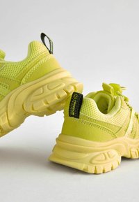 Neonowe żółte sneakersy wykonane z siatki i materiału syntetycznego, z teksturowanymi akcentami, grubą podeszwą i uchwytem z logotypem.