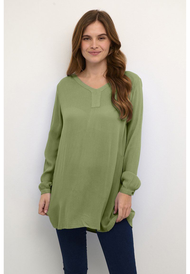 Blusa de manga larga, verde claro, con escote en V y detalles de un solo botón en los puños. Textura suave, corte relajado y diseño con dobladillo curvado.