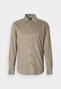 Chemise beige en velours côtelé à manches longues, avec col et poignets boutonnés sur fond blanc.