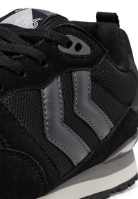 Sneaker nera che presenta una combinazione di materiali in rete e suede, con strisce grigie di accento, superfici testurizzate e una suola imbottita.
