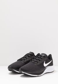 Baskets de sport noires avec une tige texturée, en matériau en maille, lacets plats et un logo Nike blanc. Dispose d'une semelle extérieure en caoutchouc durable.