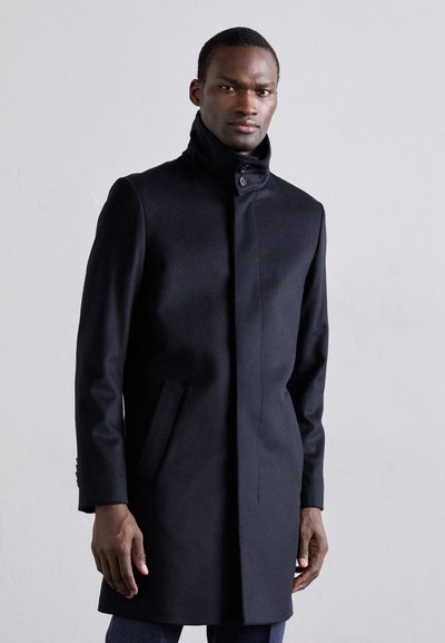 Cappotto di lana nero con colletto alto, chiusura a un bottone e due tasche laterali. Presenta un design snello e sartoriale.