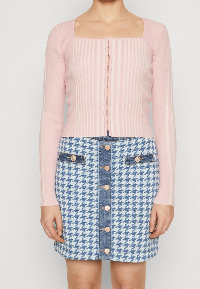 Haut à manches longues côtelé rose clair avec un décolleté carré, associé à une jupe en denim pied-de-poule bleu et blanc avec des boutons dorés.