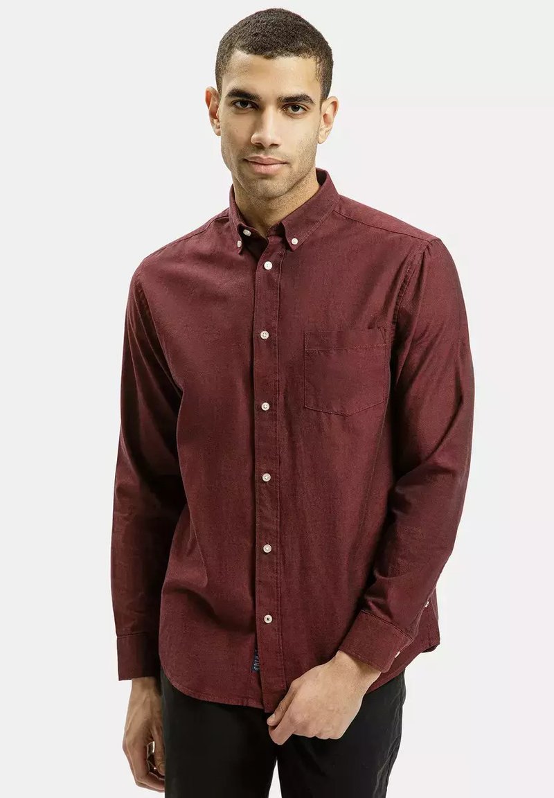 Bordowa koszula z guzikiem w teksturowanym materiale, z kieszonką, klasycznym kołnierzykiem oraz długimi rękawami. Zaprojektowana w swobodnym fasonie.