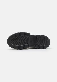Suola di scarpa in gomma nera con un motivo a zigzag, dotata di sezioni rialzate per una migliore presa e fori di ventilazione lungo il centro.