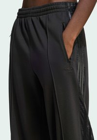 Black athletic pants with a textured material, elastic waistband, side pockets, and mesh panel accents on the outer seams.