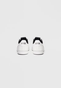 Baltos sportbačiai su lygiu odiniu paviršiumi ir juodais akcentais ant kulno. "VERSACE JEANS COUTURE" logotipas atspaustas ant nugaros. Guma padėklas.