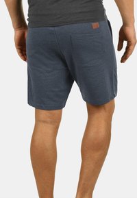 Shorts pour homme en bleu foncé, fabriqués dans un tissu doux, dotés d'une poche arrière et d'une petite étiquette en cuir près de la taille pour l'identification de la marque.