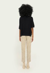 Top scurt din tricot negru, purtat cu pantaloni din corduroy bej deschis și cizme cremoase la glezne cu toc bloc. Material texturat și croială lejeră.